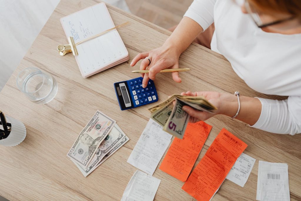 Overhead view of a person using a calculator to manage cash and receipts at a desk.